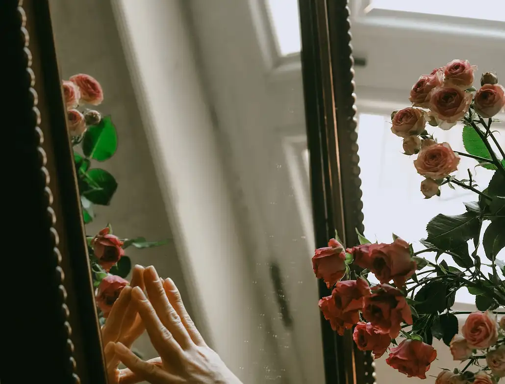 Main d'une femme qui regarde son corps dans un miroir avec des roses